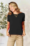 Smiling model wearing a women's basic black t-shirt with crew neck and short sleeves paired with tan pants