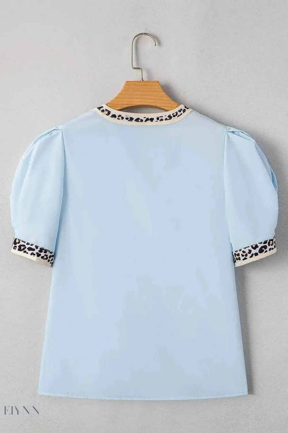 Light blue leopard trim puff sleeve blouse back view on a hanger showing puff sleeves and leopard trim neckline and cuffs