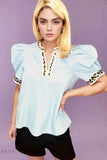 Woman wearing light blue leopard trim puff sleeve blouse with scalloped hem and black shorts