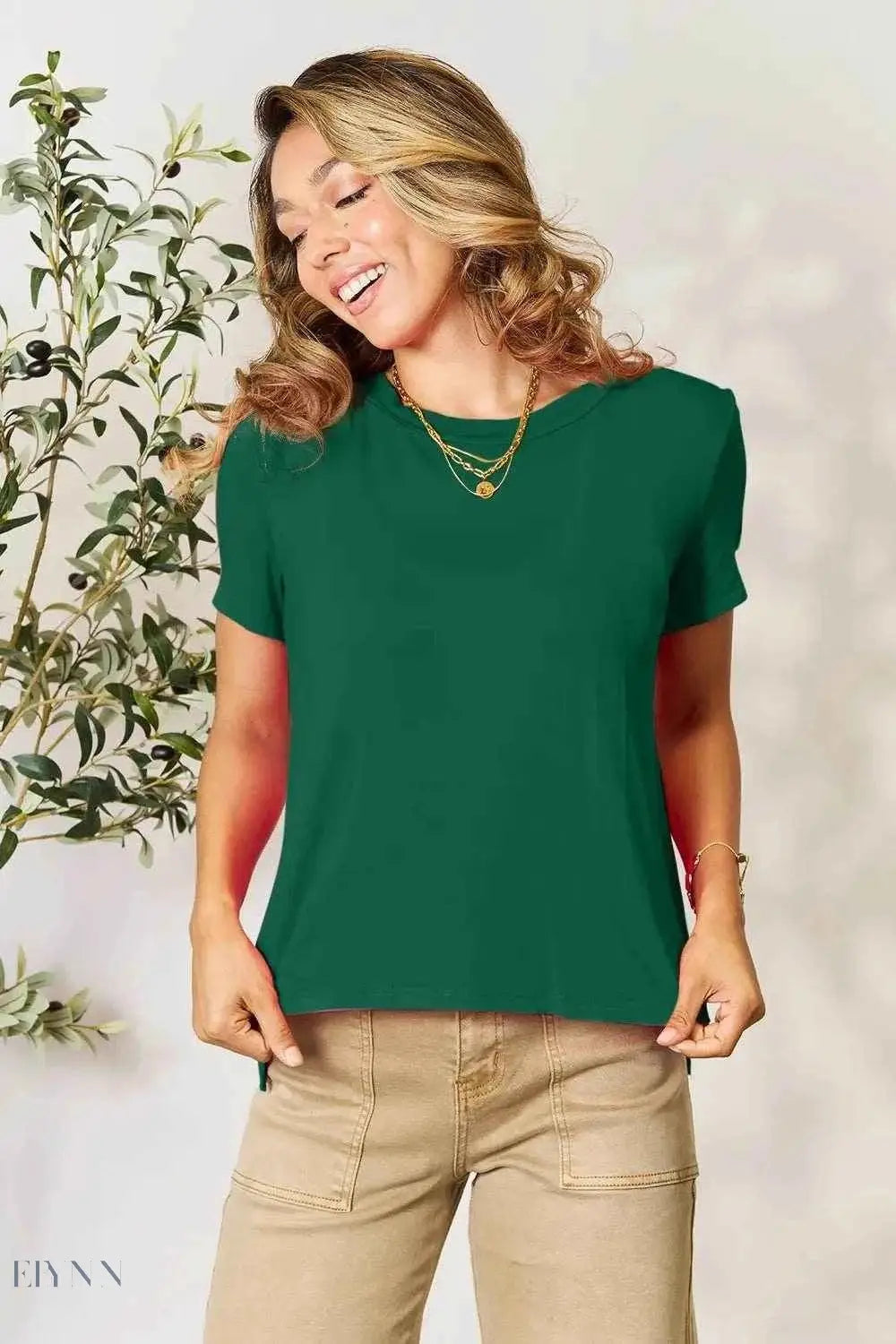 Model wearing green crewneck tee and khaki pants holding hem for women's basic black t-shirt listing