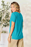 Trendsi model smiling in a teal t-shirt and beige pants posed back view for women's basic black t-shirt